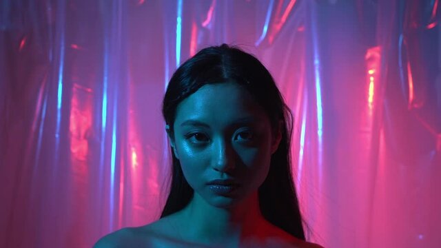 pretty asian young woman looking at camera on neon pink and blue