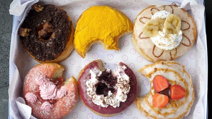 A finger picking out the jam filling from the berry donut. Selection of bitten donuts in a box