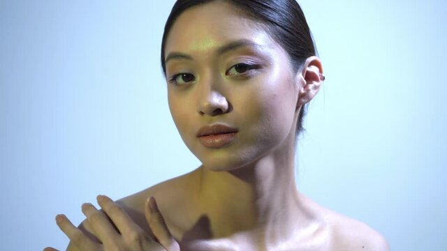 young asian woman with bare shoulders touching clavicle on blue