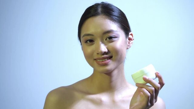 happy young asian woman holding container with cream on blue