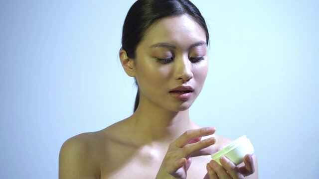 pretty asian woman applying cream on soft skin on blue