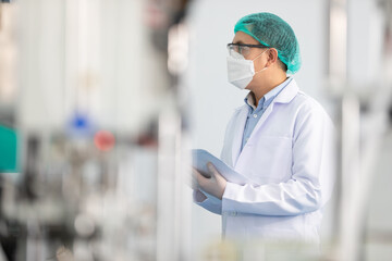 factory worker wearing medical face mask and checking production line for quality control from machine