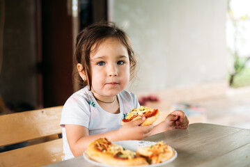 A girl, a child on the street eats a mini pizza very appetizing