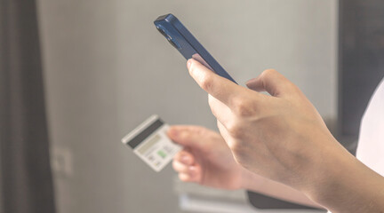 Lady use mobile phone for order online and pay bills with credit card in living room interior at home. Smartphone and credit card in hand close-up, banner photo