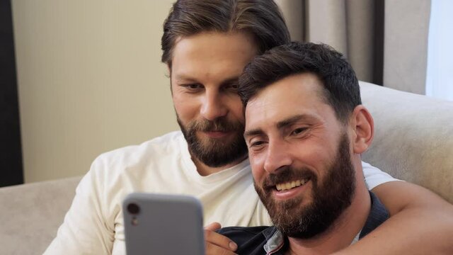 Guys Smile and Laugh in Love. Cute Male Homosexual Gay Couple Spend Time Together at Home. Men Taking Selfie on Smartphone Hugging Each Other. LGBTQI, Pride Event, LGBT Pride Month, Gay Pride Symbol.