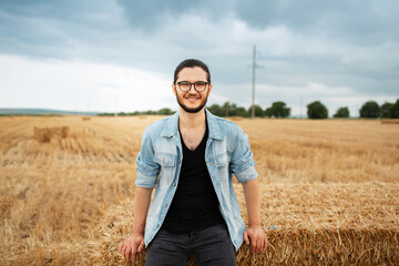 Naklejka na ściany i meble Portrait of happiness young guy standing near haystacks in wheat field.