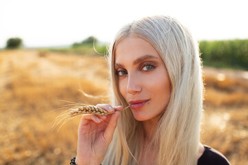 Close-up portrait of young cute blonde girl with wheat spike in mouth.