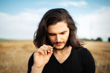 Portrait of young man with long hair and wheat spike in the mouth.