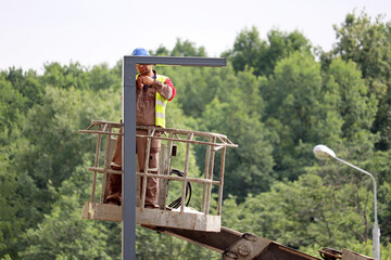 Electrician repairing the street light with led lamp. Worker standing on the lifting platform near...
