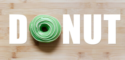 Donut word with green donut instead of 'O' letter, on wooden table.