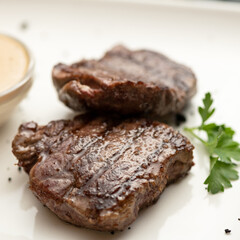 Grilled tenderloin, juicy steak or meat fillet with herbs and mustard on white plate. Close-up shot. Soft focus.
