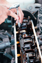 Car service. An auto mechanic repairs a car engine. Internal combustion engine valve adjustment. Close-up on the engine and hands with the tool.