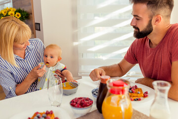 Parents feeding baby boy and having breakfast