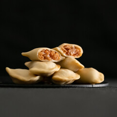 Hot boiled dumplings with stewed cabbage filling on black background. Cooked dumplings cross section. Convenience Food, dough stuffed. Close-up shot. Soft focus. Side view. Square format. Copy space.