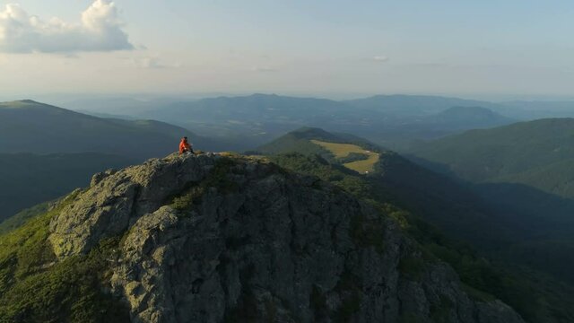Male hiker sitting on top of rocky mountain peak, looking down the deep valley