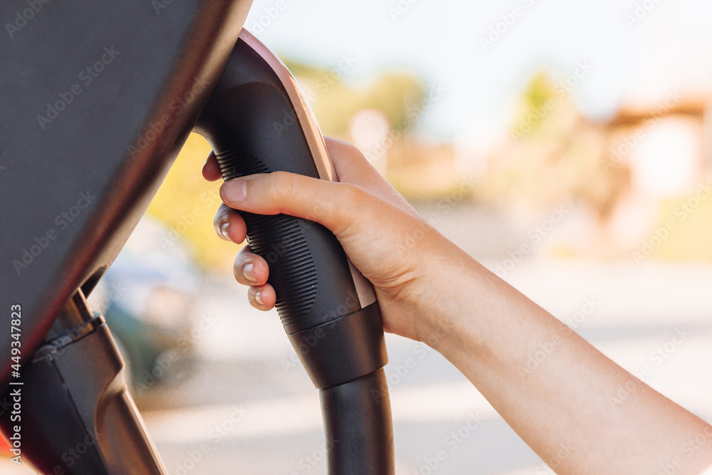 Wall mural woman's hand holding an electric vehicle or ev car socket in a charging station. the future of the a