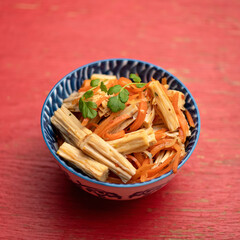 Thai salad with carrots and celery. Bowl of eastern food on red background. Soft focus.