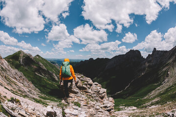 Obraz premium Successful woman backpacker hiking on sunset alpine mountain peak