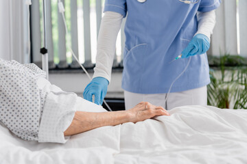 Obraz na płótnie Canvas Cropped view of nurse holding catheter near senior woman on hospital bed
