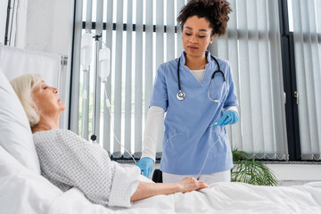 African american nurse holding catheter near elderly patient in clinic