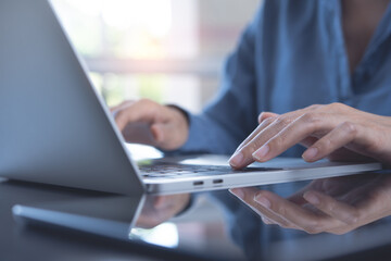 Closeup image of a business woman's hands working and typing on laptop keyboard on glass table with reflection