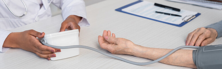 Cropped view of african american doctor holding tonometer near patient in clinic, banner