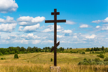 Cross of the Russian Orthodox Christian Church in the middle of a field, a picturesque landscape with fields and a blue sky