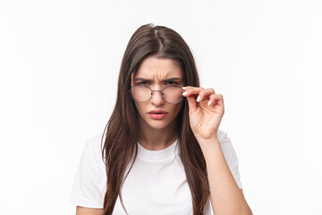Close-up portrait of suspicious young serious-looking woman, look from under glasses, squinting at person with judgemental disbelief stare, standing white background, have doubts - obrazy, fototapety, plakaty