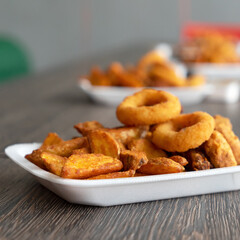 Crispy snack for Beer. Fried potato chips and rings on blurred background. Side view. Close-up shot. Copy space.