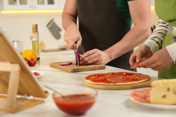 Couple making pizza together while watching online cooking course via tablet in kitchen, closeup