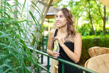  young woman smiling and posing in a summer cafe. happy young woman holding a glass of ice cocktail on a hot summer day in a cafe.