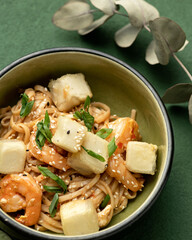 Spicy oriental noodles or spaghetti with shrimp vegetables and sesame seeds. Close-up of bowl with Asian food. Pan-Asian cuisine. Soft focus. Vertical format.