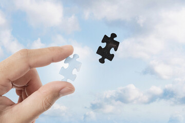 Hand filling piece of jigsaw puzzle. on the sky