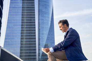 Businessman reading email received on a modern tablet while sitting outdoors in front of an office...