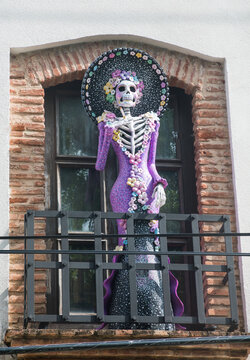 dramatic image of a skeleton mannequin wearing a  colorful dress and hat smoking a cigarette, in colonial district of santo domingo, Dominican Republic.