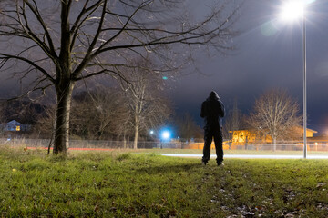 A hooded figure, silhouetted against a street light on the edge of town at night
