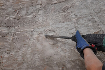 Worker remove, demolish old tiles and mortar from wall using electric hammer and chisel in a...