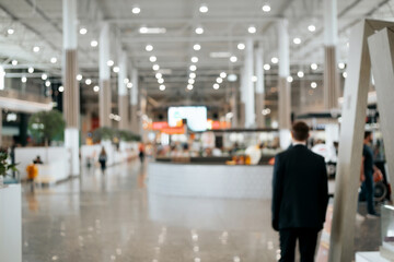 Defocused shopping mall background, large illuminated hall, security guard rear view. Blurred...