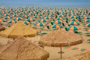 View of a sand beach full of colorful sun umbrellas without people during a sunny summer day 