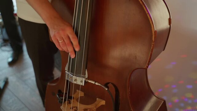 Man playing a stringed electronic musical instrument. Unrecognizable male person play the electric cello violin indoors closeup