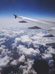 Fototapeta premium Beautiful window view of blue sky and fluffy clouds from passenger seat on airplane. View of many windmills at big green meadows. Concept of travel and air transportation.