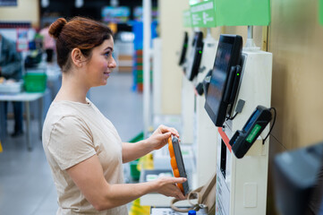 Caucasian woman uses a self-checkout counter. Self-purchase of groceries in the supermarket without...