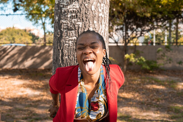 Retrato de chica sacando la lengua apoyada en un árbol en el parque.