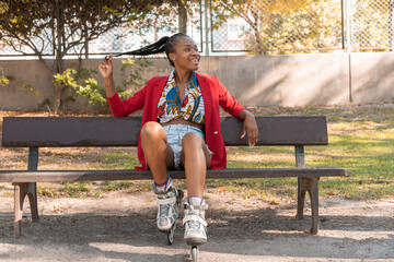 Chica africana sentada con patines, en un banco en el parque con expresión de felicidad.