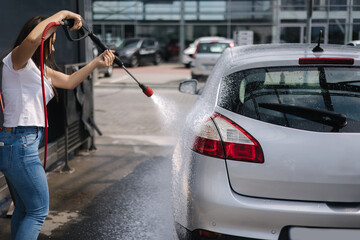 Back view of young woman cleaning her car on self service car. Female washing with jet sprayer....