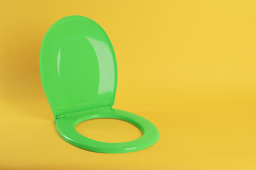 New green plastic toilet seat on yellow background, space for text