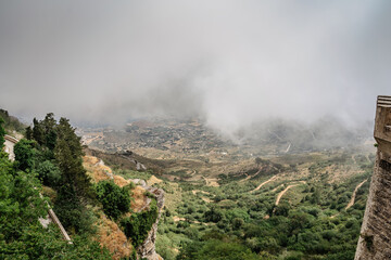 Fototapeta premium View from Erice, Sicily, Italy. Historic town on the top of mountains overlooking landscape and sea.View of beautiful lush countryside in clouds. Breathtaking panorama. Misty landscape with curvy road