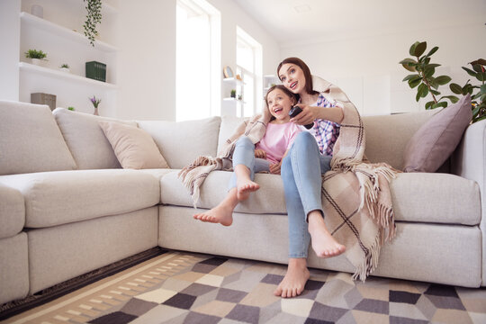 Full length photo of cheerful happy positive pretty sisters siblings watch tv sit sofa indoors inside house home