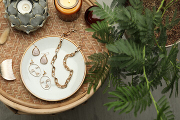 Stylish golden bijouterie and candles on wicker table, top view