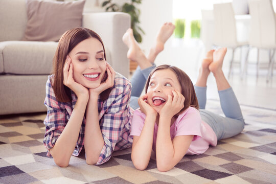 Portrait of two attractive cheerful girls lying on floor having fun good mood fooling at home flat indoors